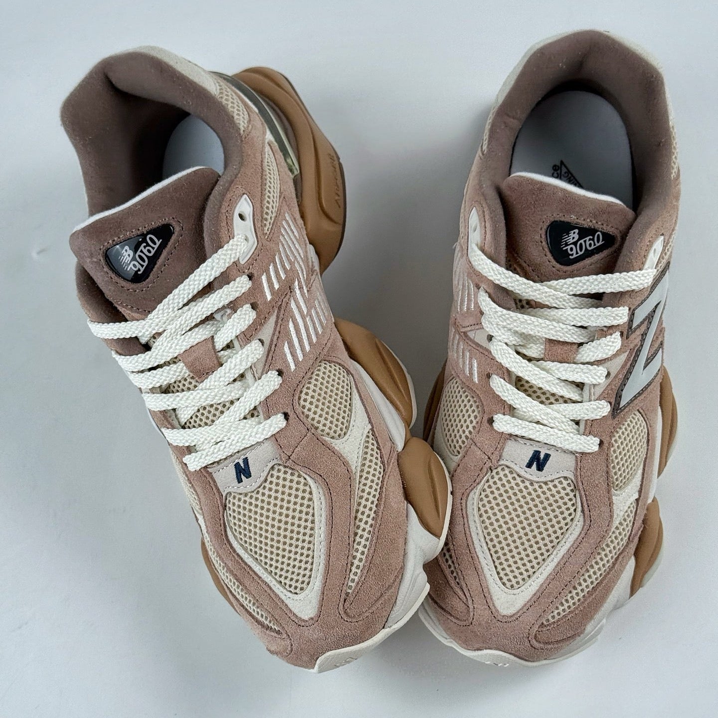 Pair of brown and beige sneakers with white laces on a light gray background
