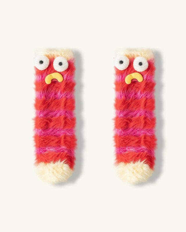 Pair of red and pink fuzzy socks with googly eyes and a yellow mouth on a white background